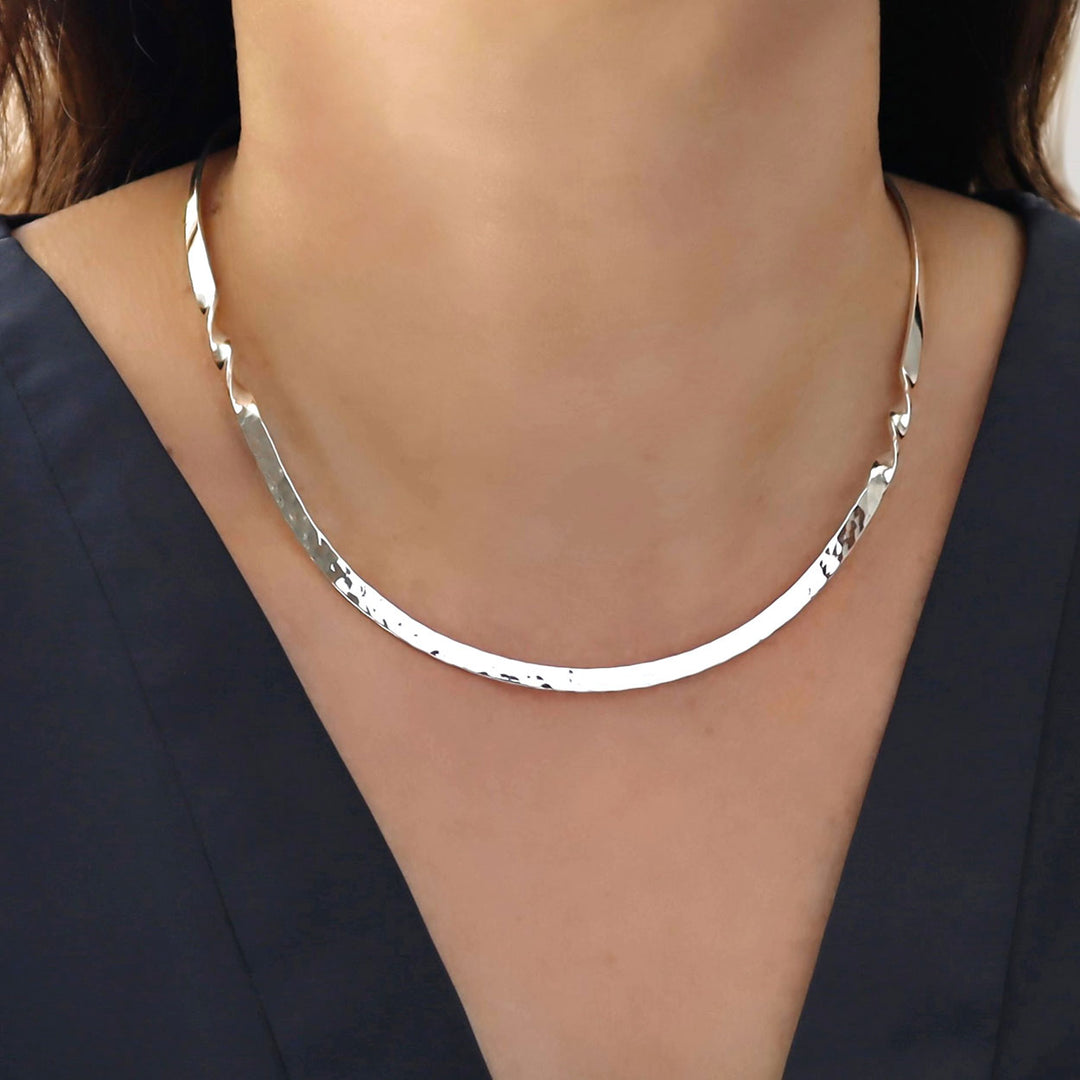 Silver choker style necklace worn by a person against a dark background