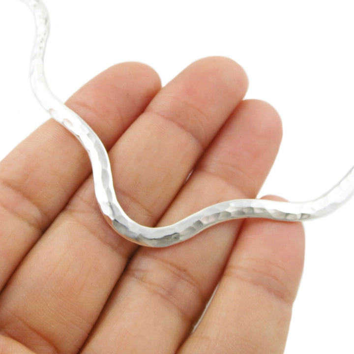 A close-up of a hand holding a wavy, hammered sterling silver choker necklace against a plain white background.