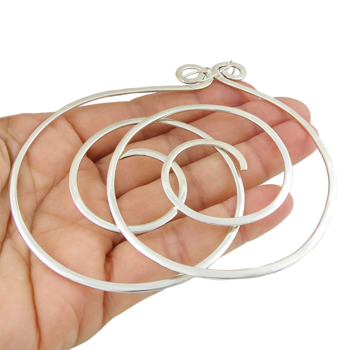A large pair of women's spiral hoop earrings in 925 sterling silver held in a person's hand on a white background.  