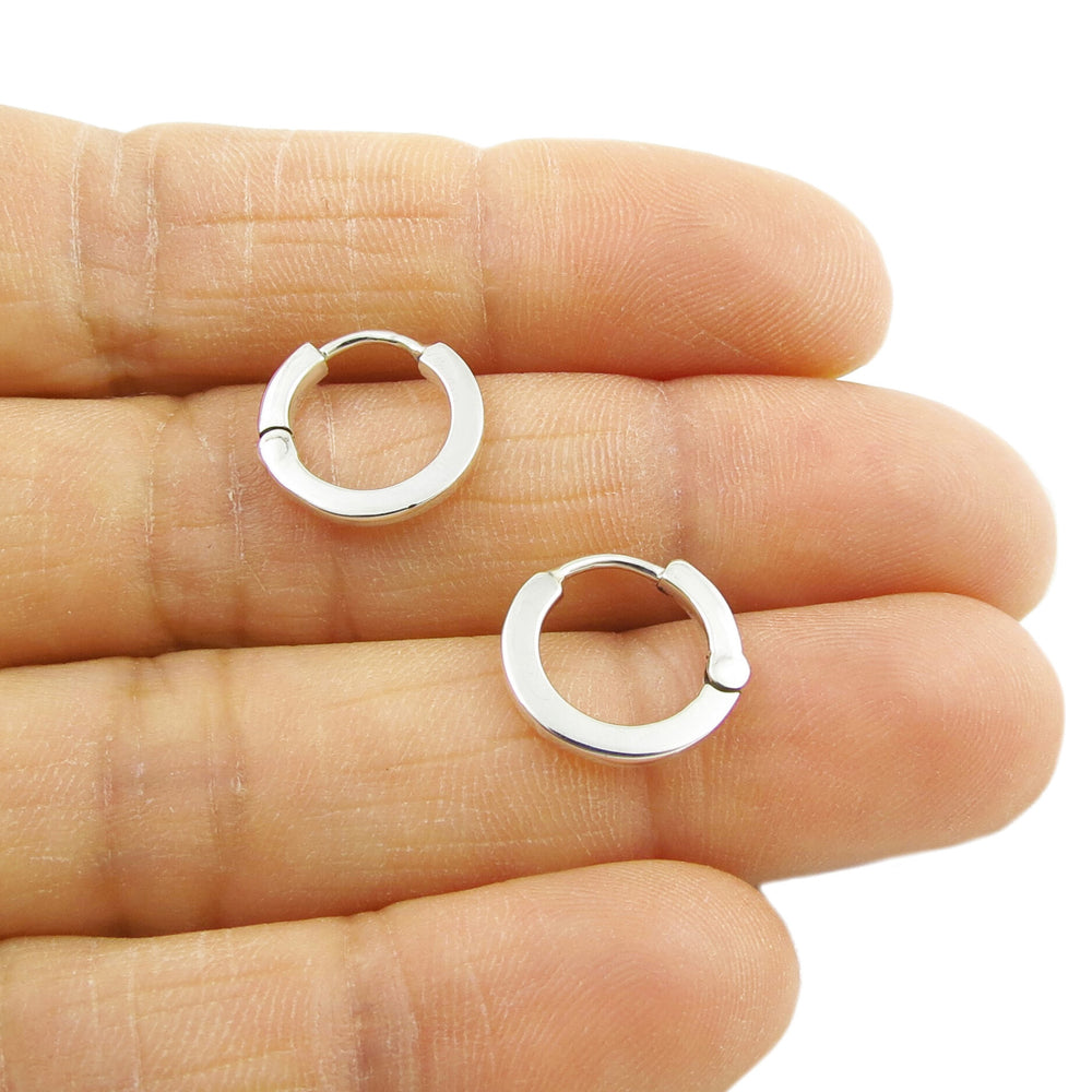 A pair of small 925 silver hinged hoop earrings ideal for stacking held between fingers.