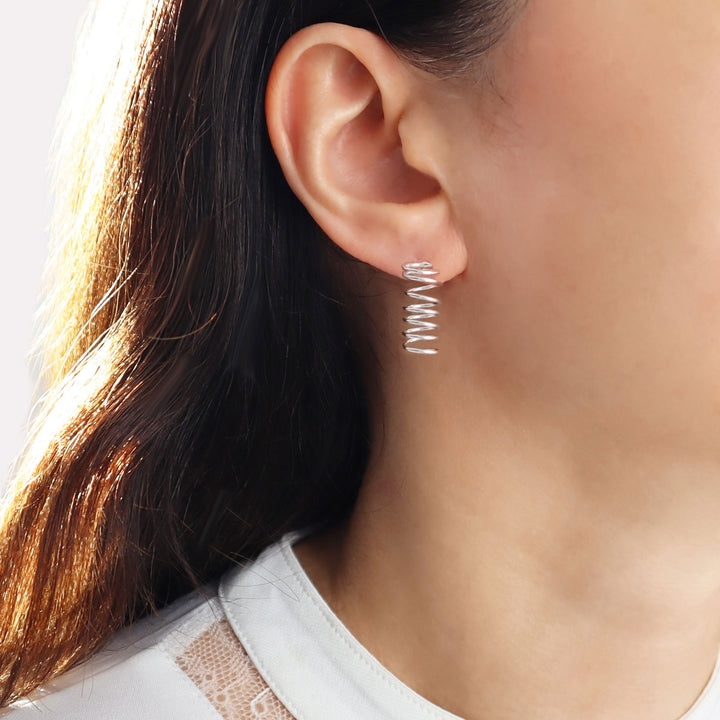 Close-up of an ear wearing long spiral earrings.