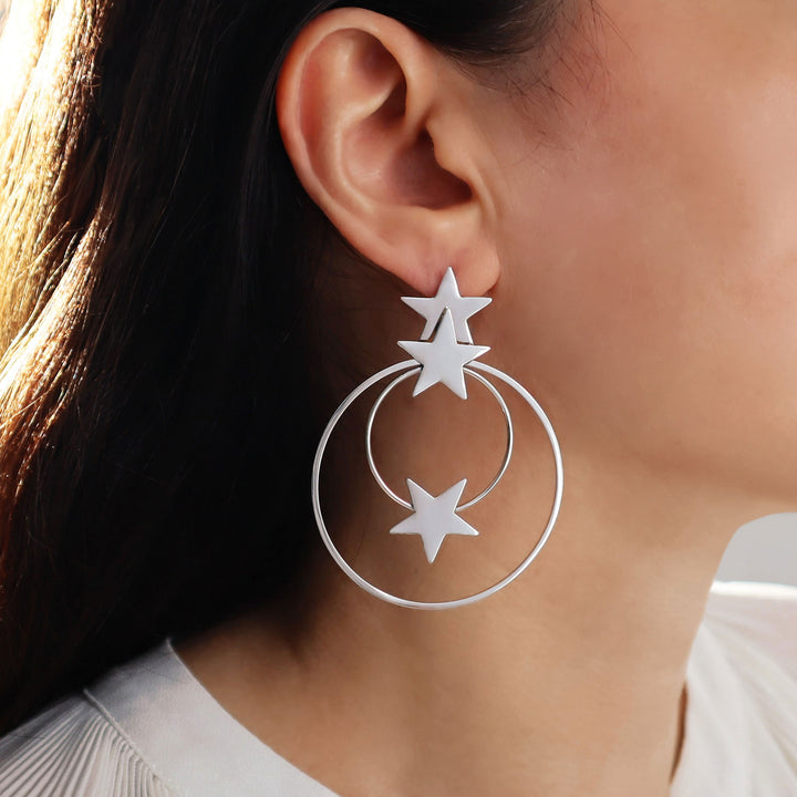 Large silver hoop earrings with star designs worn by a person.