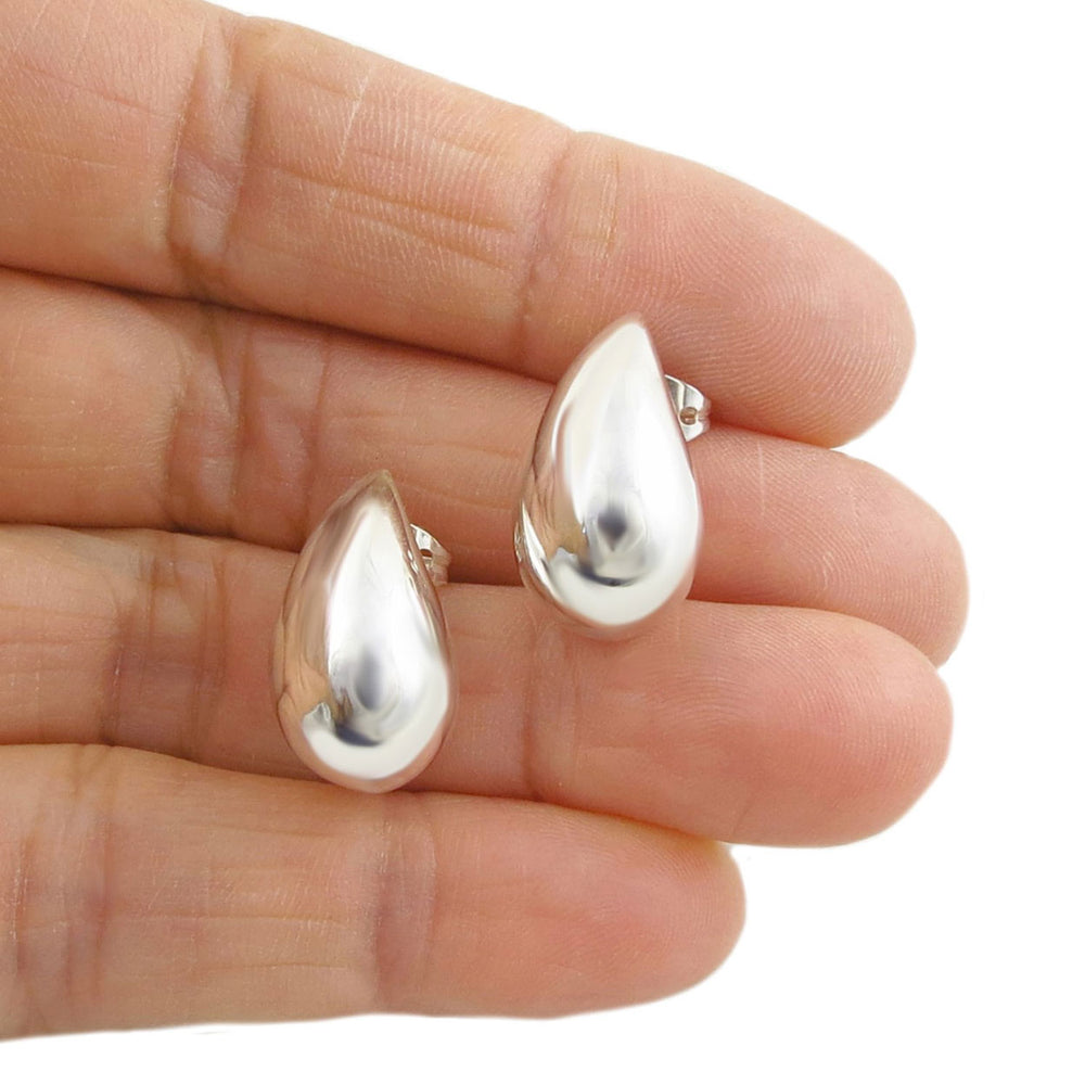 A pair of large silver teardrop stud earrings held in a person's hand.