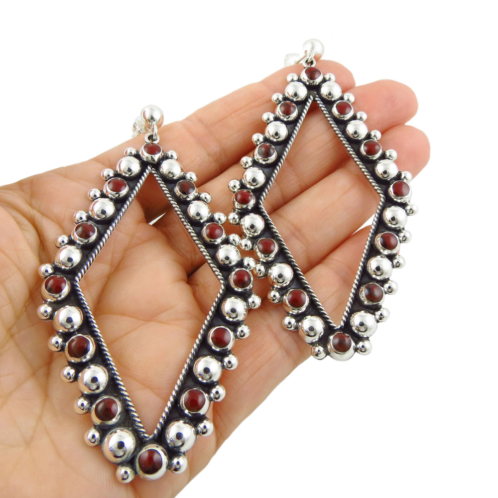 Statement diamond-shaped hoops with red stones held in a person's hand