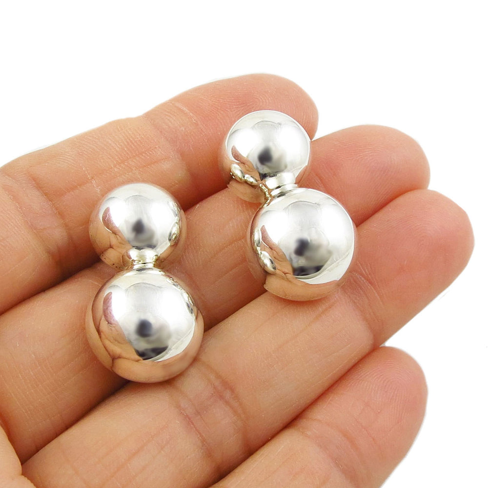 Long double ball sterling 925 silver drop earrings held in a woman's hand on a white background. 