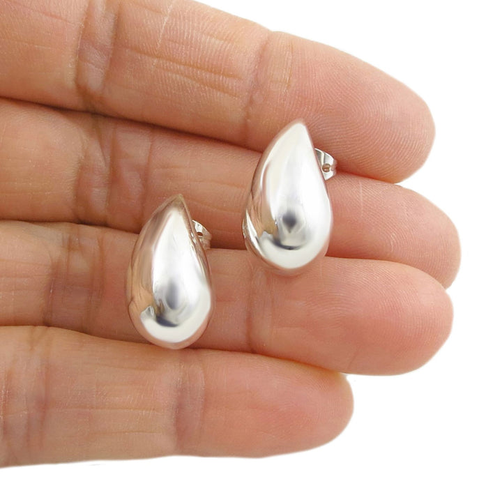 Long 925 silver teardrop ladies stud earrings held between fingers on a white background