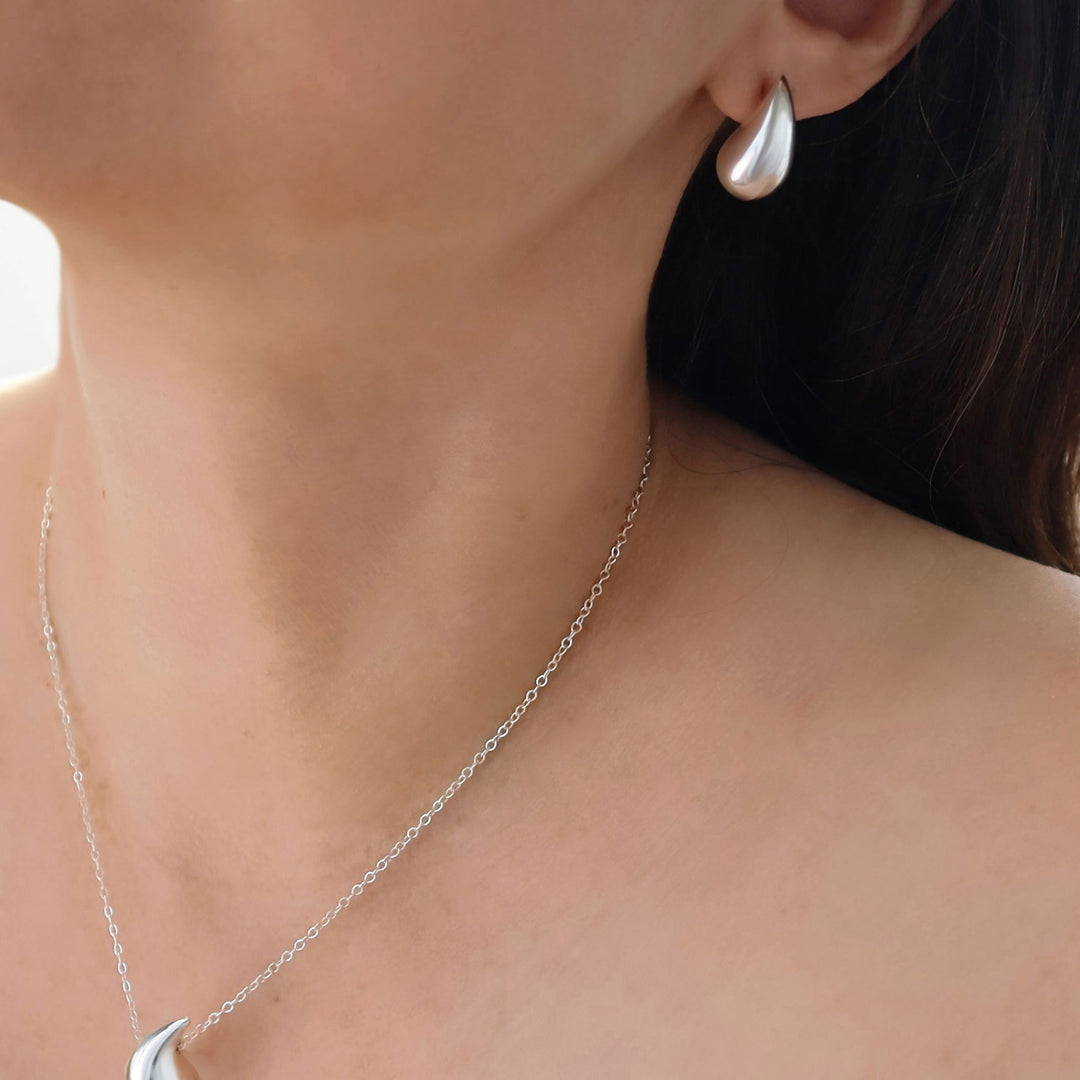 Close-up of a woman wearing a 925 polished silver stud earring and a chain necklace