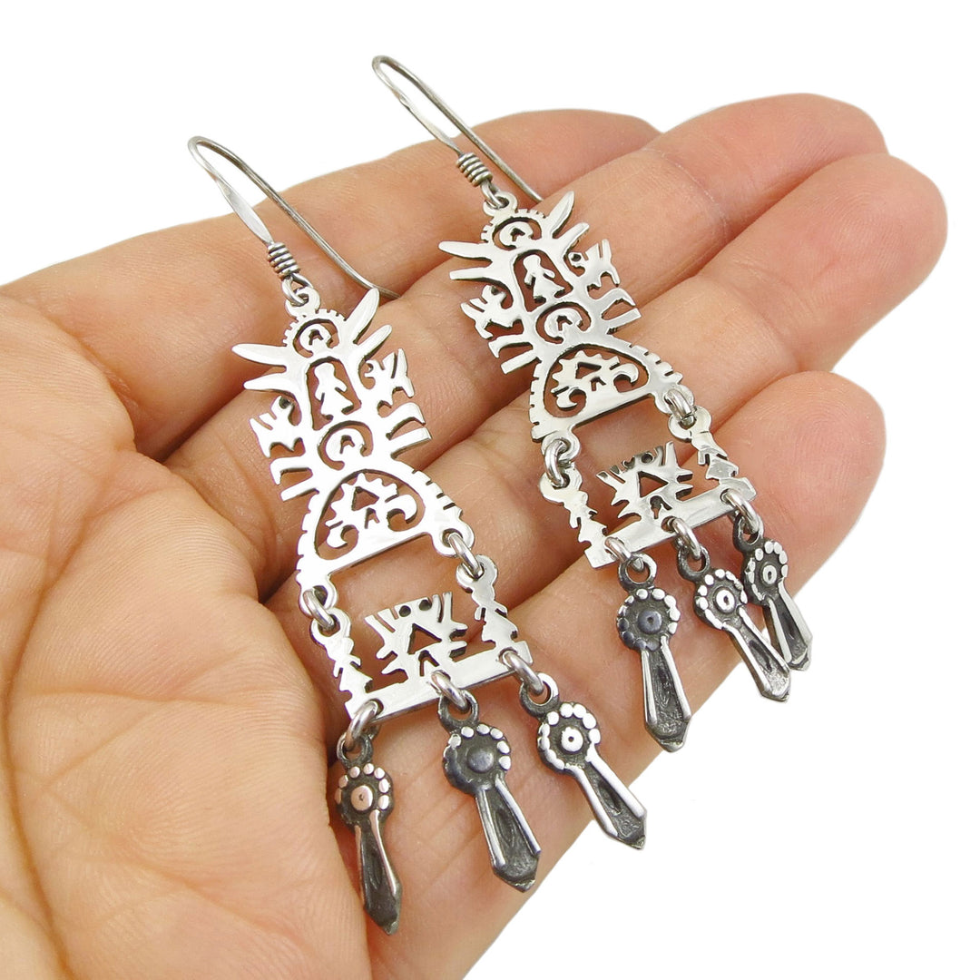 Mexican 925 sterling Silver daangling earrings with an intricate tree of life design held in a hand against a white background