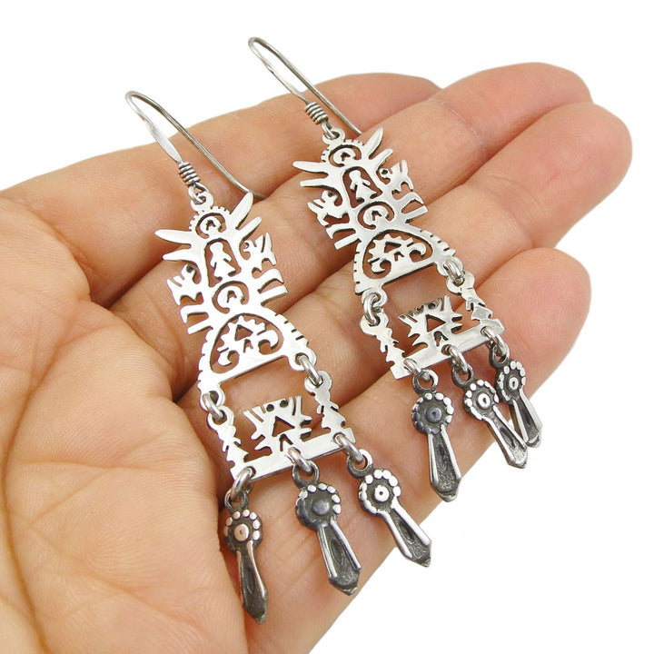 Mexican 925 sterling Silver daangling earrings with an intricate tree of life design held in a hand against a white background