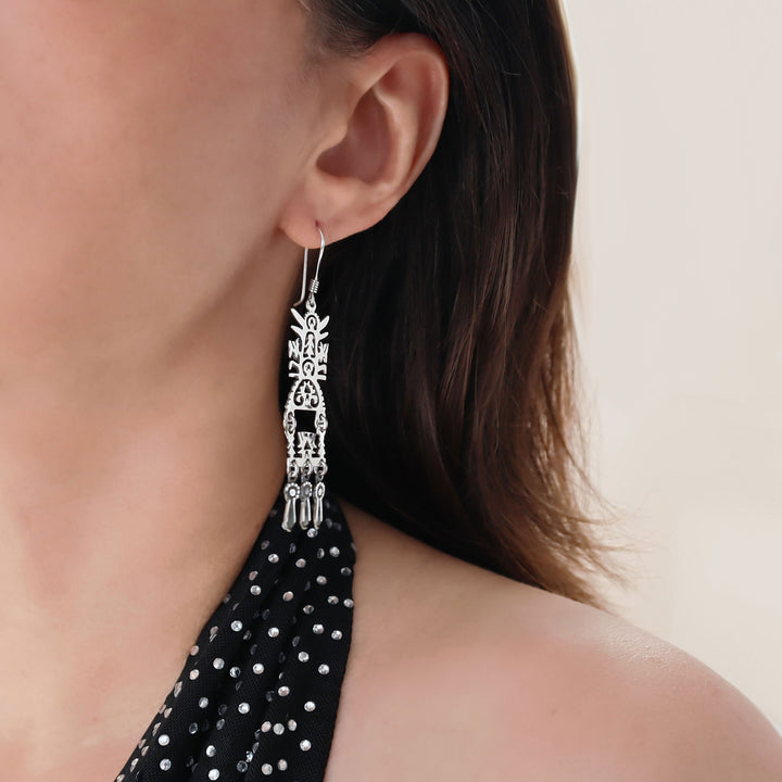 Close-up of a woman wearing a long dangling chanderlier tree of life design 925 sterling silver earring with a black and white polka dot top.