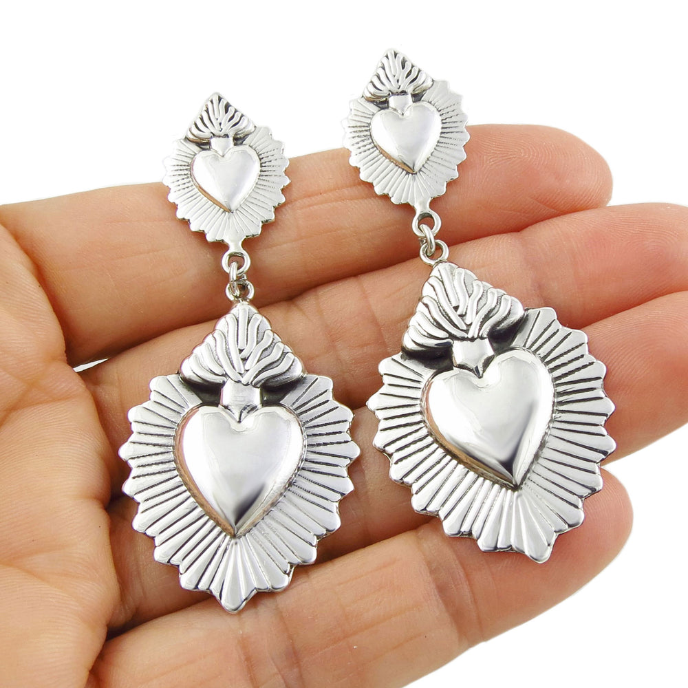 Flaming heart design silver earrings held in a persons hand
