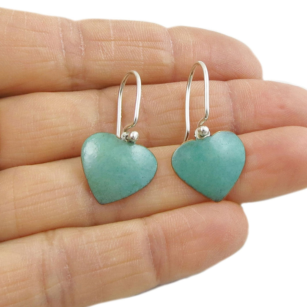 Copper heart earrings held in a prson's hand. 