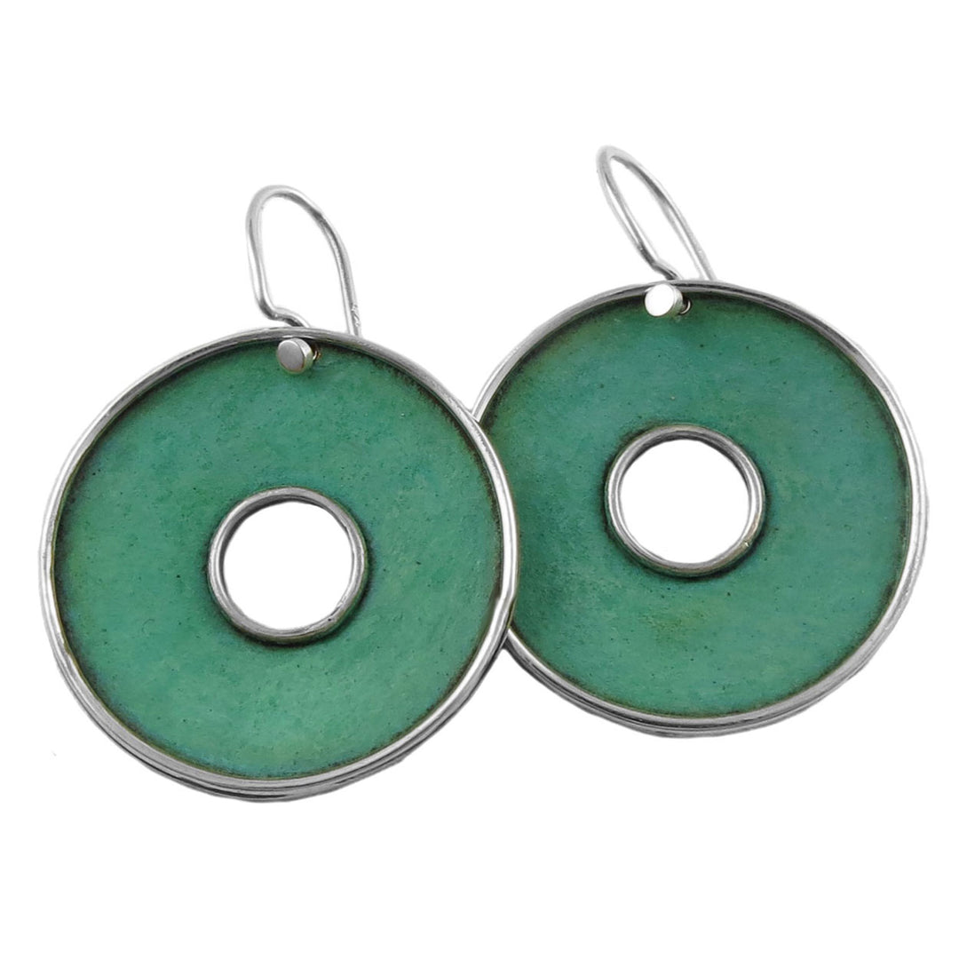 A pair of large round patina copper hoop earrings with green coloring and a central hole, attached to hooks for wear.