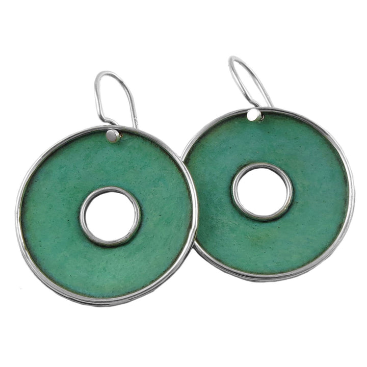 A pair of large round patina copper hoop earrings with green coloring and a central hole, attached to hooks for wear.