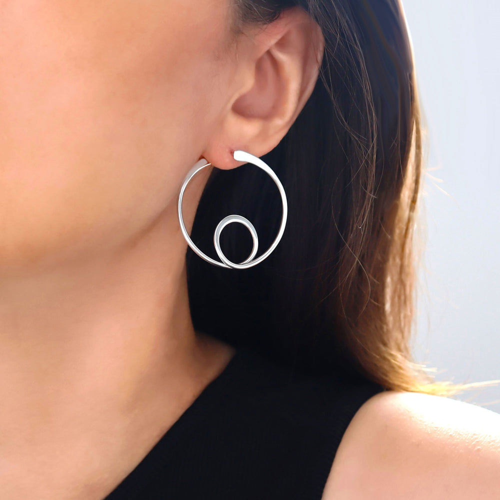 A close-up image of a woman's ear wearing a silver hoop earring, showcasing the front and back of the earring design.