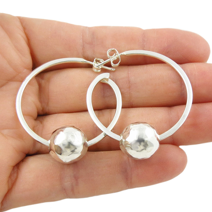 Large sterling 925 silver gypsy hoop earrings with spherical ball beads held in a woman's hand on a white background