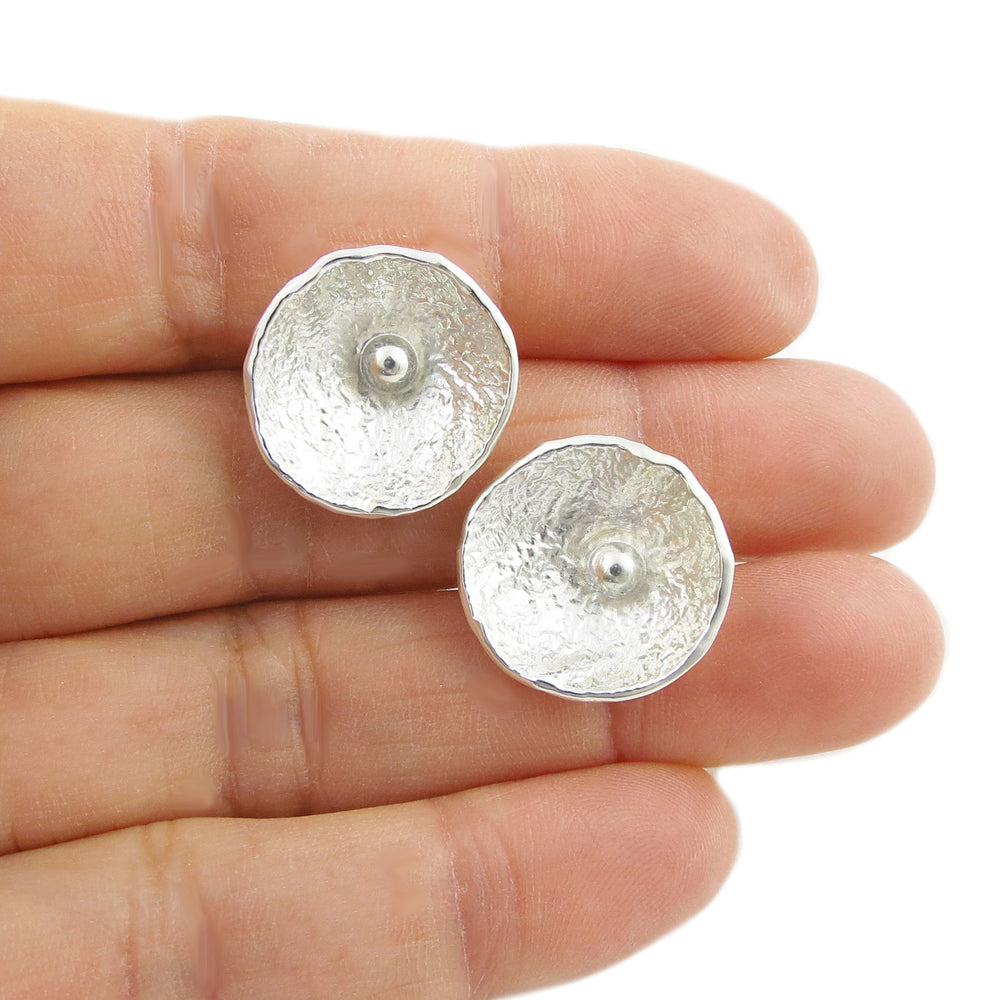 Silver poppy flower earrings held between fingers on a white background