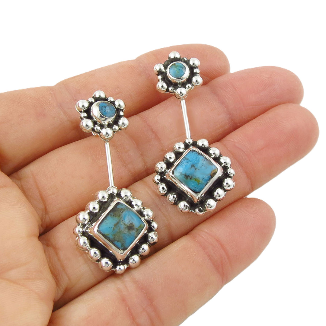 Turquoise and silver earrings held in a hand against a white background