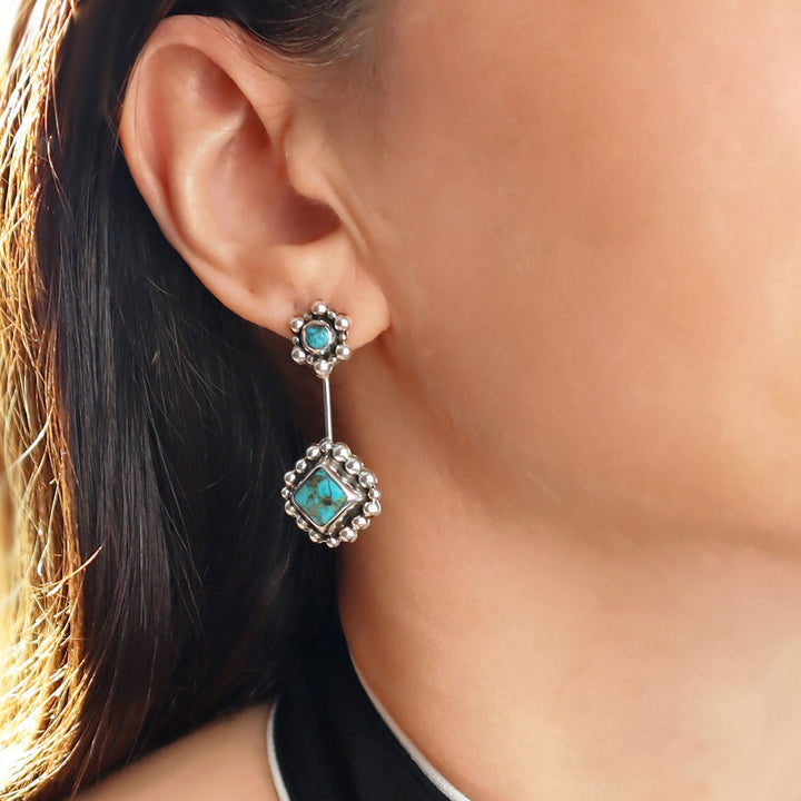 Close-up of a person wearing a turquoise drop earring with a silver setting.