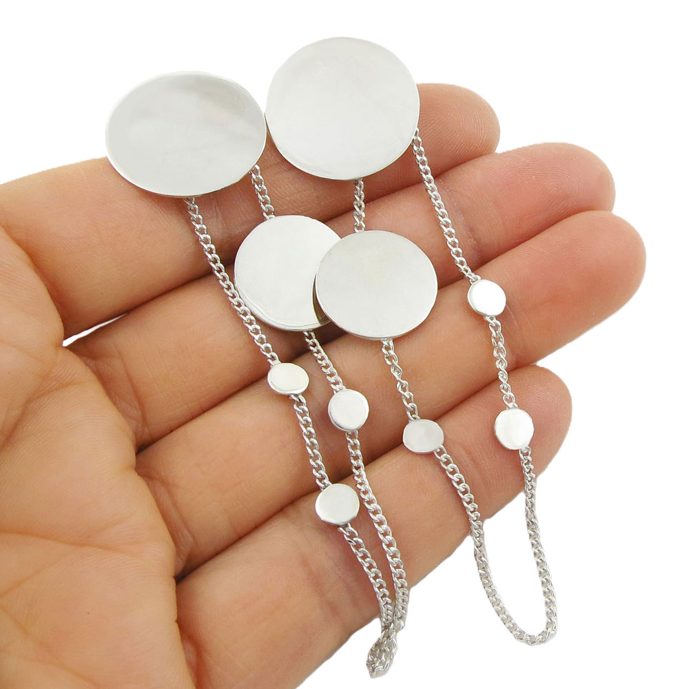 Silver chain earrings with round polished discs held in a hand against a white background
