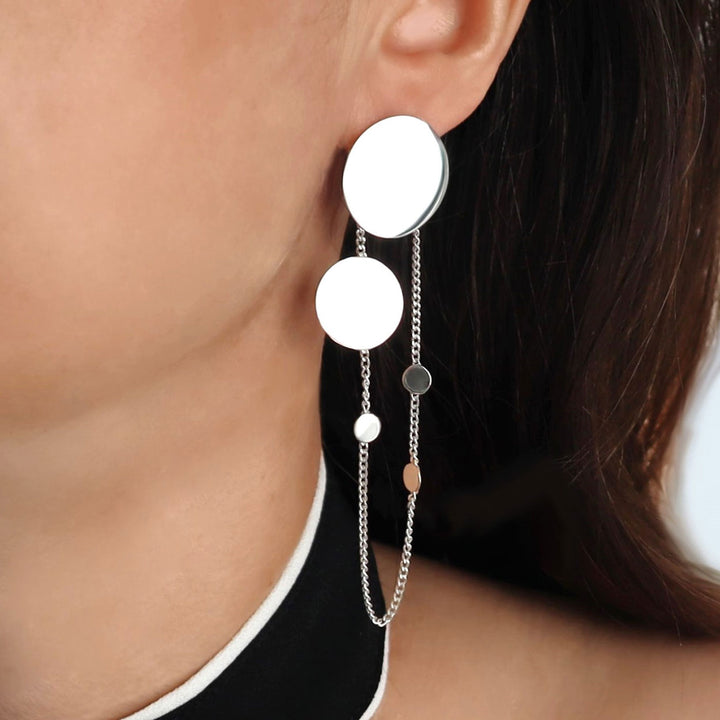 Close-up of a person wearing a silver earring with circular elements and a chain.