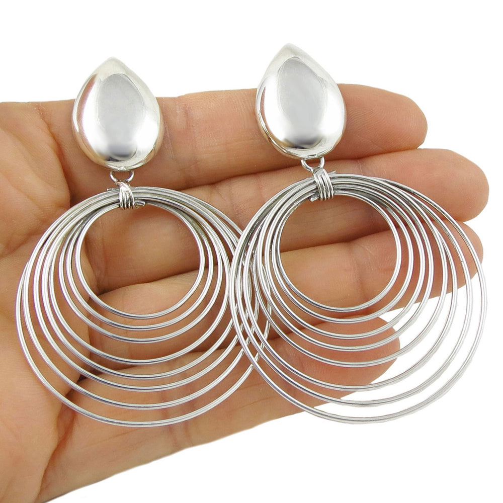 Large 925 silver spiral hoop earrings held in a hand against a white background
