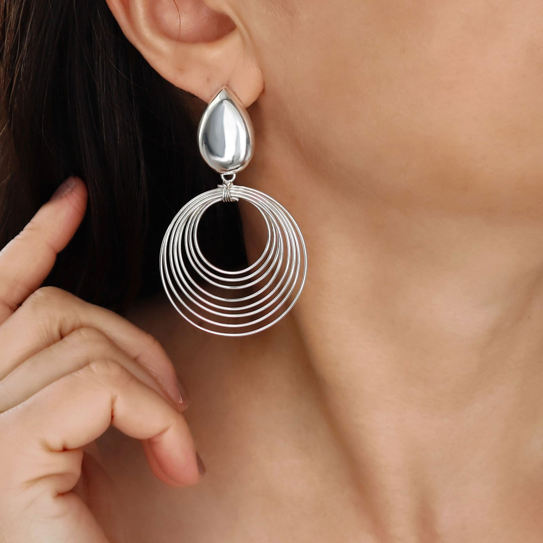 Long silver drop earring worn by a person with a blurred background