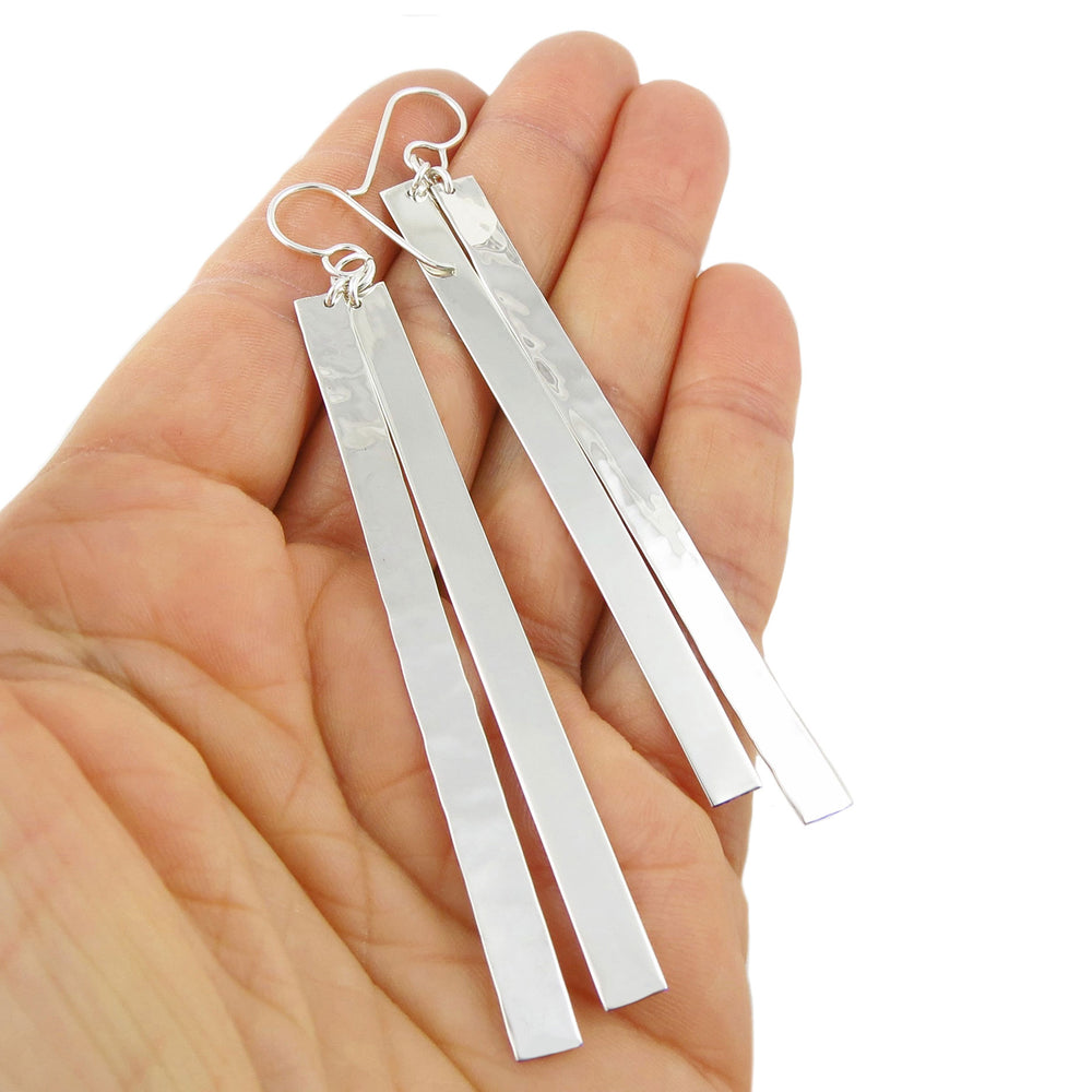 Silver double bar earrings held in a hand against a white background