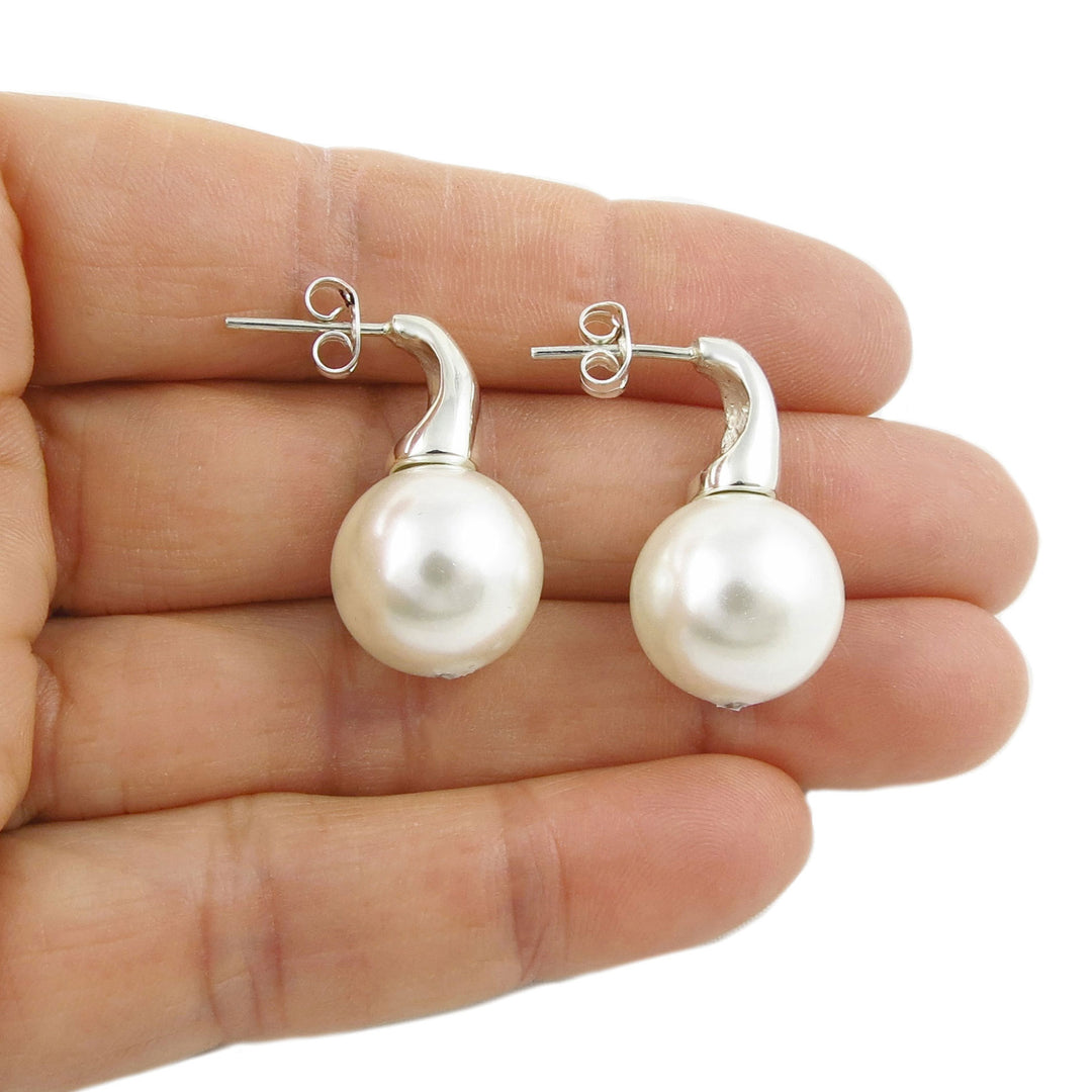 Pearl earrings held between fingers on a white background