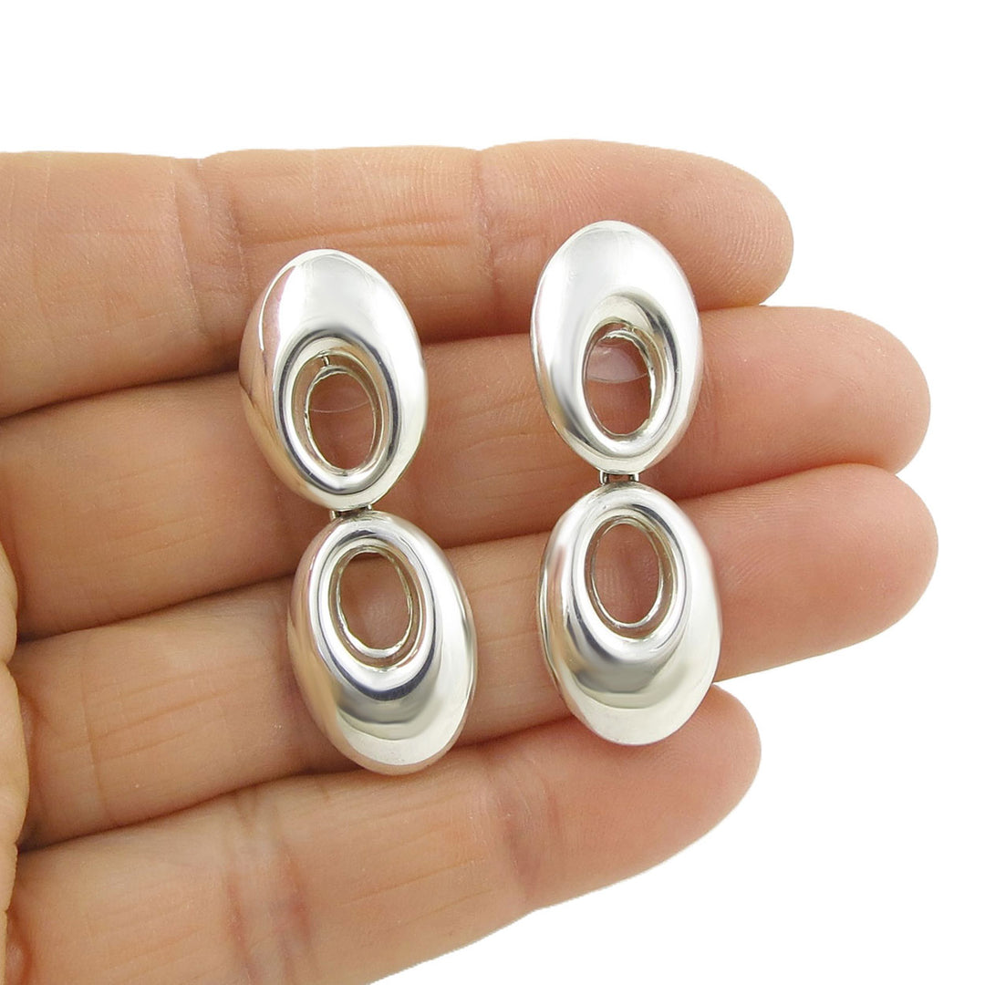 Silver Maria Belen Nilson earrings held between two fingers on a white background