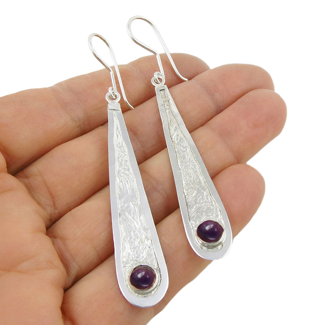 Crushed 925 silver earrings with purple amethyst natural gemstones held in a hand on a white background