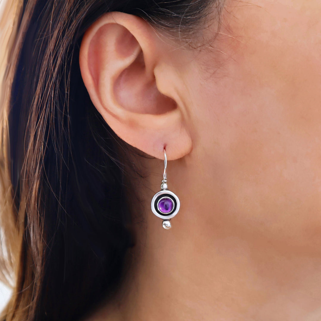 Close-up of an ear wearing a silver earring with a purple amethyst gemstone.