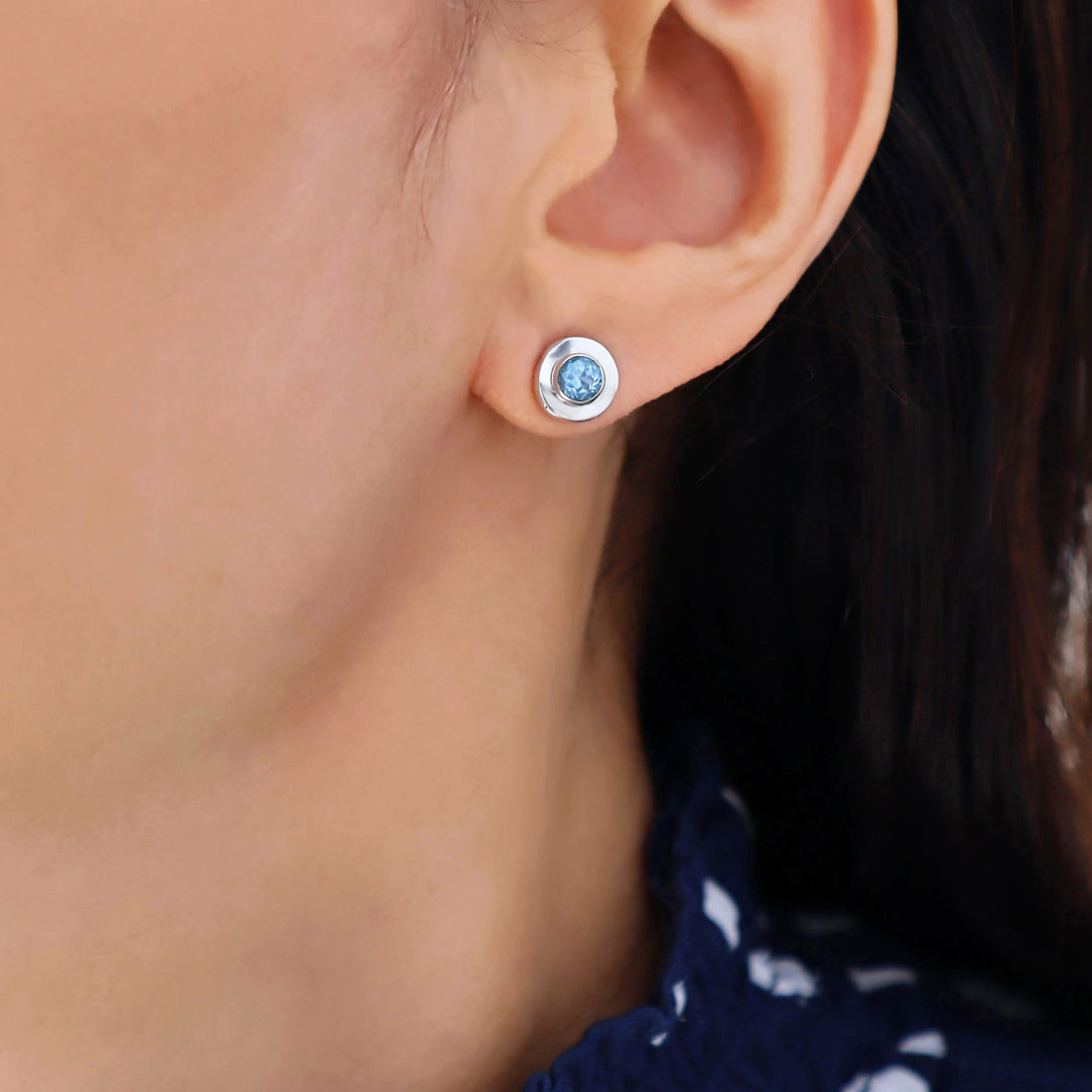 Close-up of an ear wearing a silver earring with a faceted blue topaz gemstone.