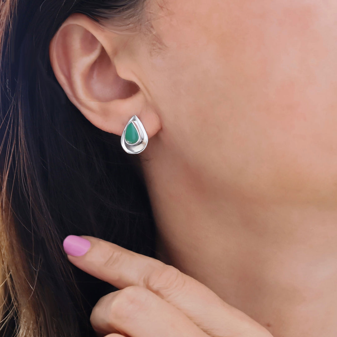 Teardrop-shaped silver and green gemstone earring worn by a person with a blurred background