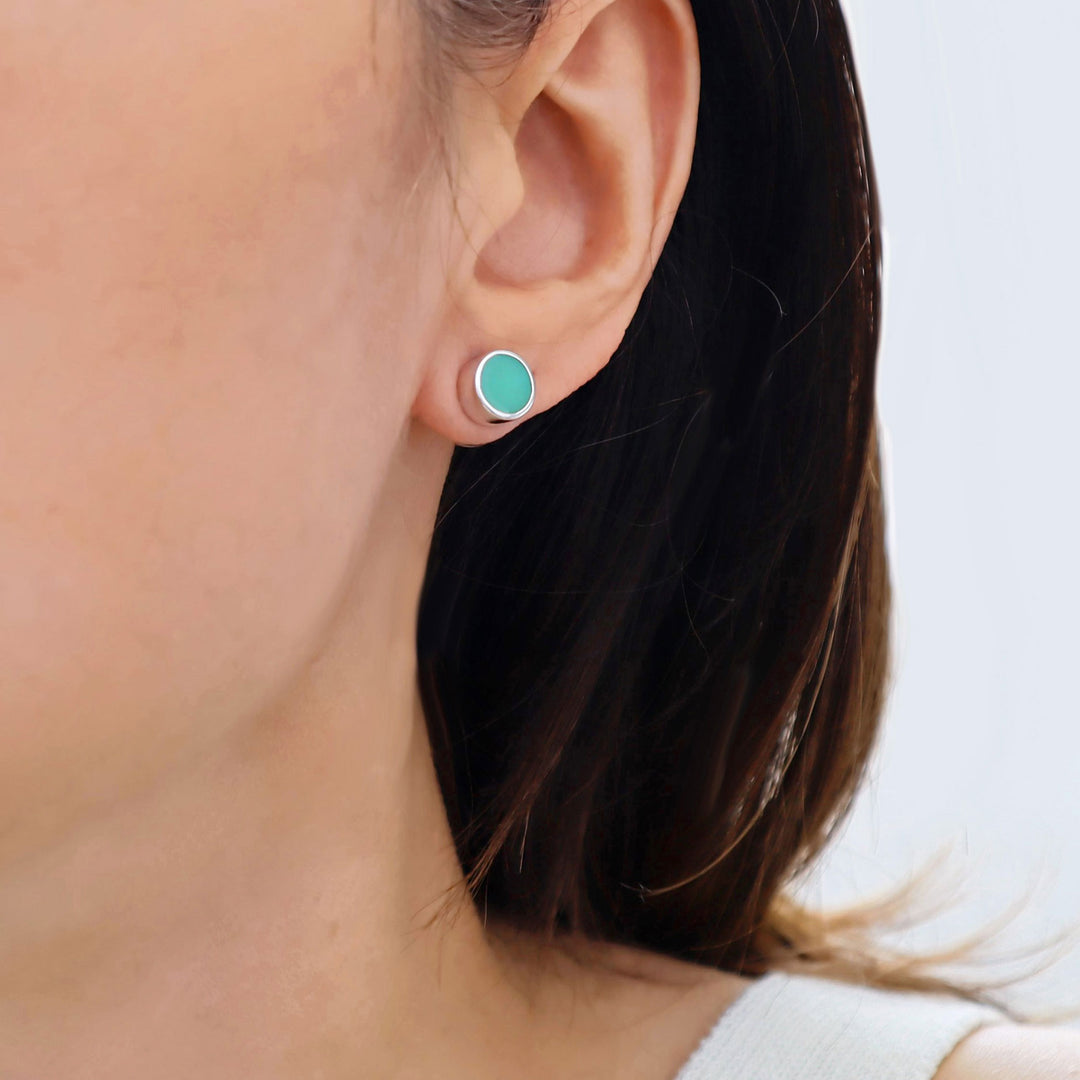 Close-up of a person wearing a green gemstone stud earring on a plain background