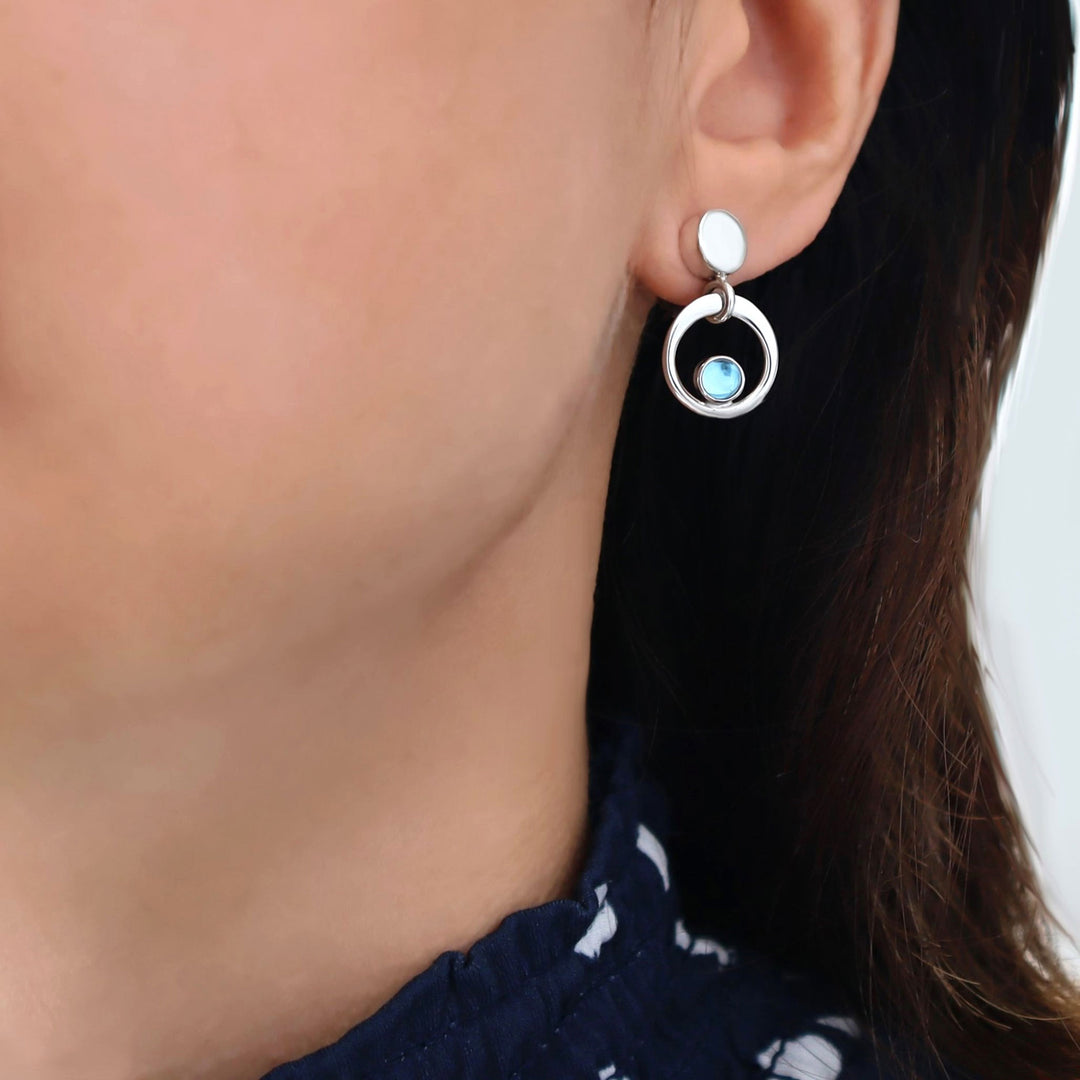 Close-up of a person wearing a silver earring with a blue topaz birthstone.