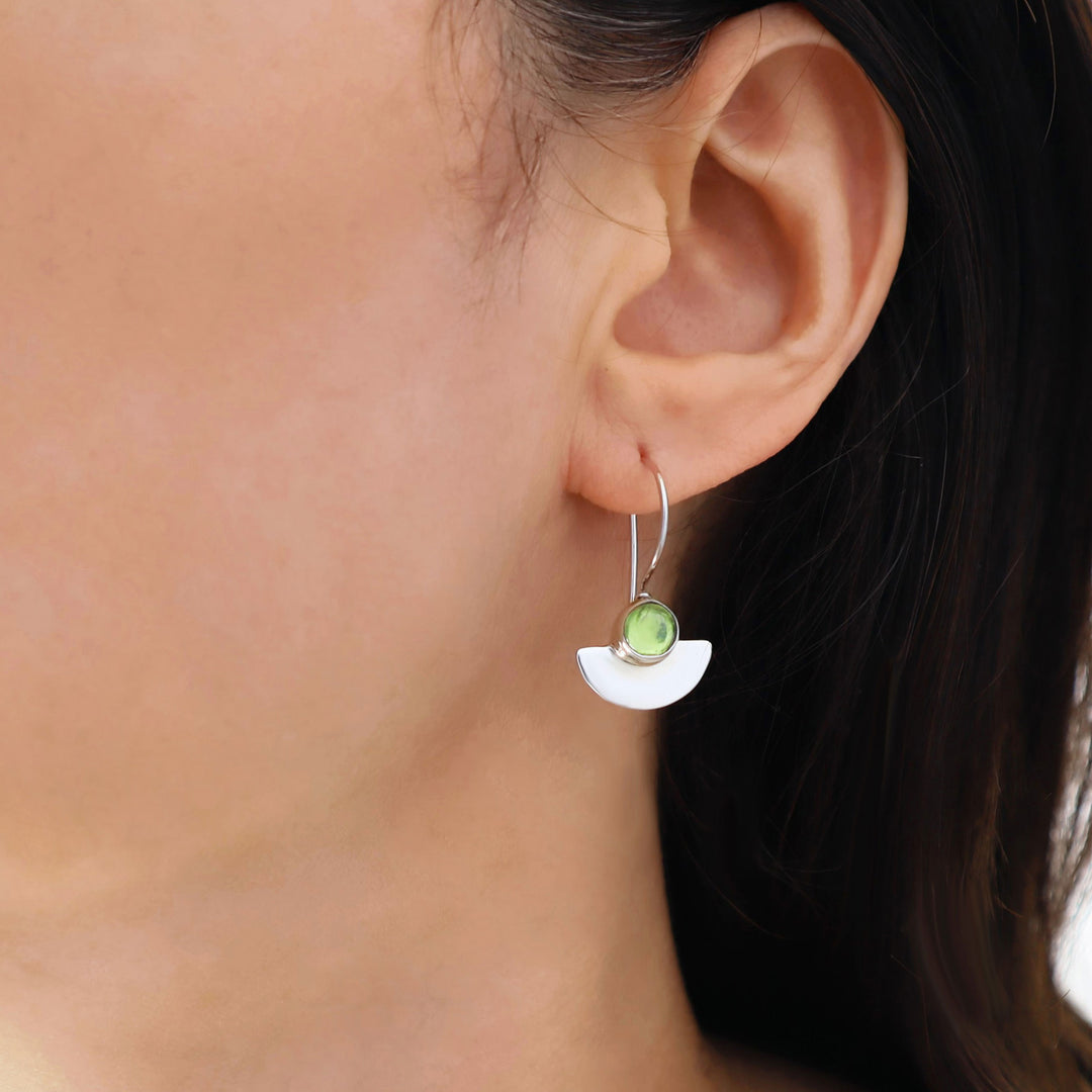 Close-up of an ear wearing a silver earring with a green peridot gemstone.
