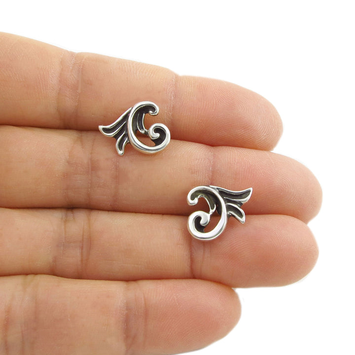 Silver flower earrings held between fingers on a white background