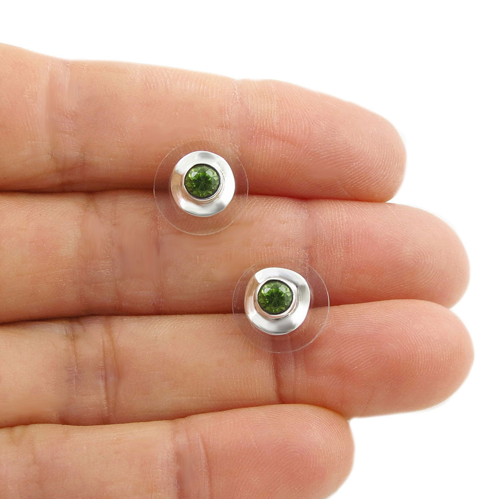 Two silver earrings with green peridot gemstones held between two fingers on a white background