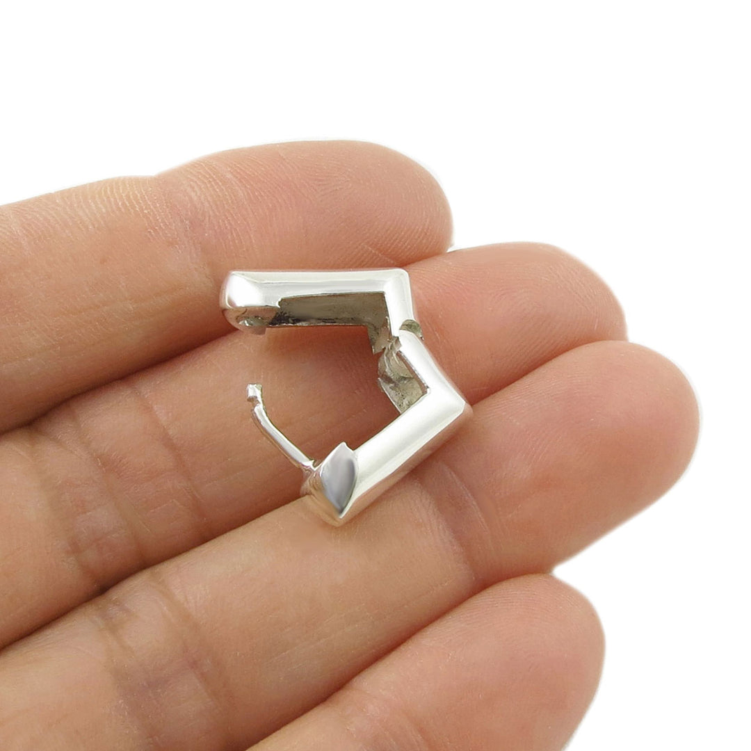 A single open silver huggie hoop earring held between fingers on a white background