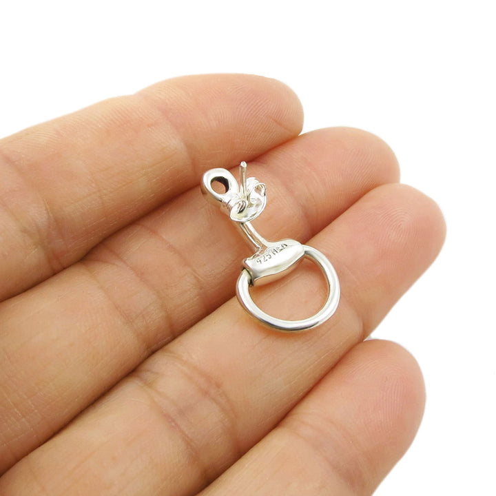 Silver equestrian-themed earring held between fingers on a white background