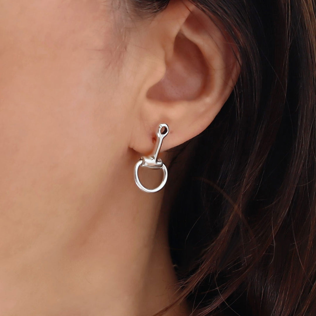 Silver horsebit earring worn on an ear with a blurred background