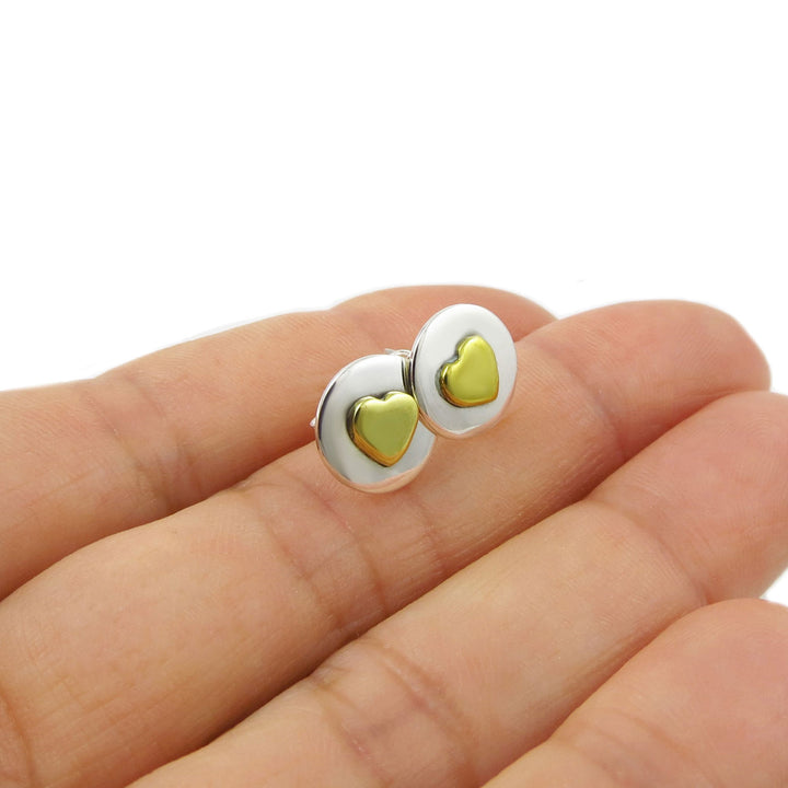 Gold heart-shaped earrings held between fingers on a white background