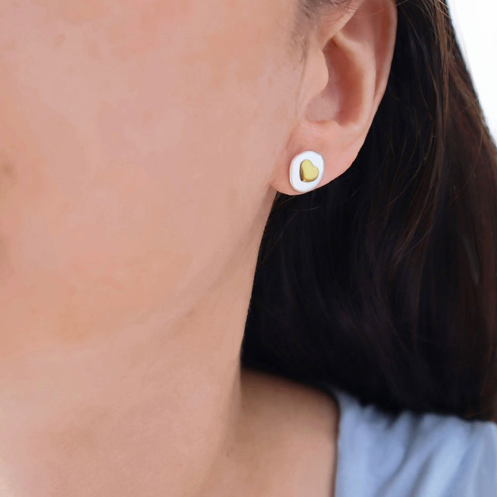 Close-up of an ear wearing a heart-shaped earring with a gold center.
