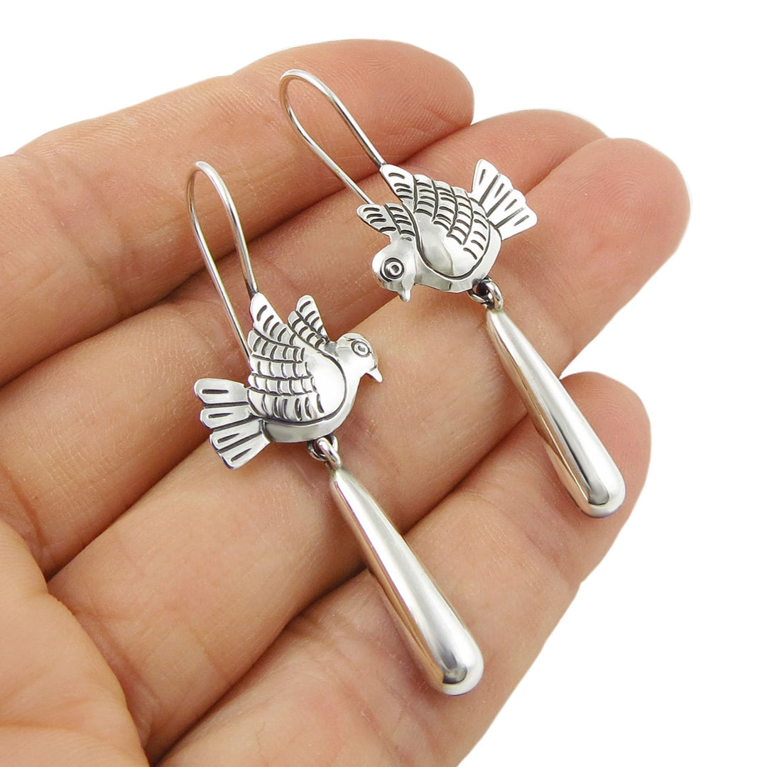 Silver dove-shaped earrings held in a hand against a white background