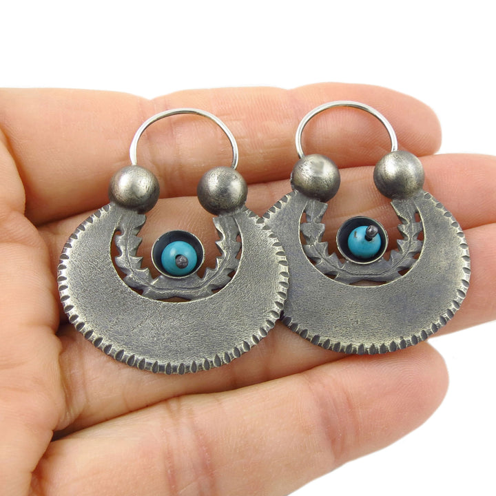 Large 925 sterling Silver exclusive Maria Belen Nilson earrings with blue natural turquoise gemstones held in a hand against a white background