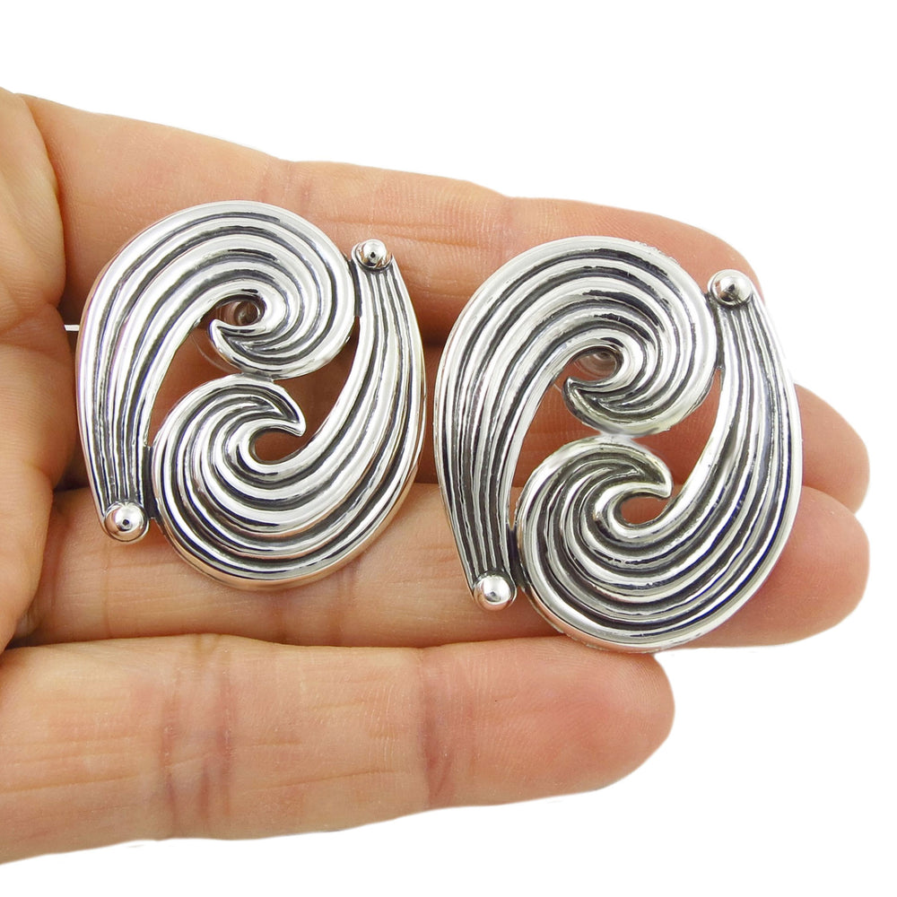 Large silver spiral earrings held in a hand against a white background