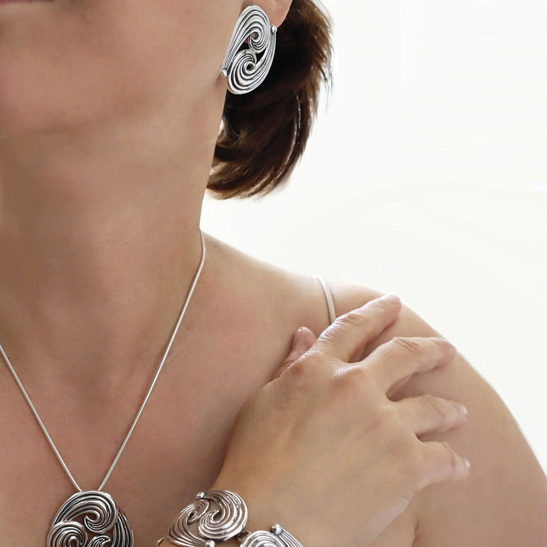 Silver jewellery set including matching earrings, necklace, and bracelet on a model against a white background. 
