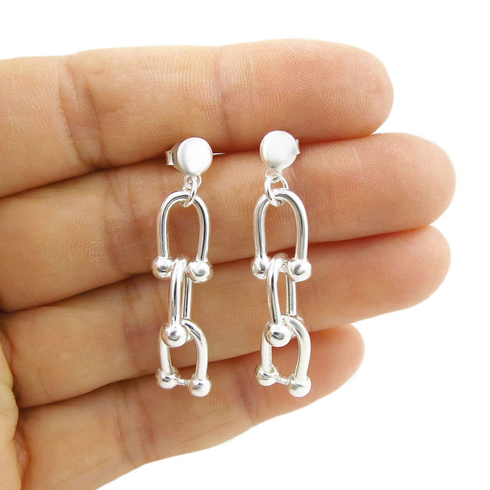 Silver gauge link chain earrings held between fingers on a white background