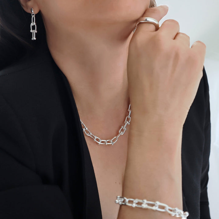 Close-up of a woman wearing silver jewellery including guage link chain earrings, necklace and bracelet.